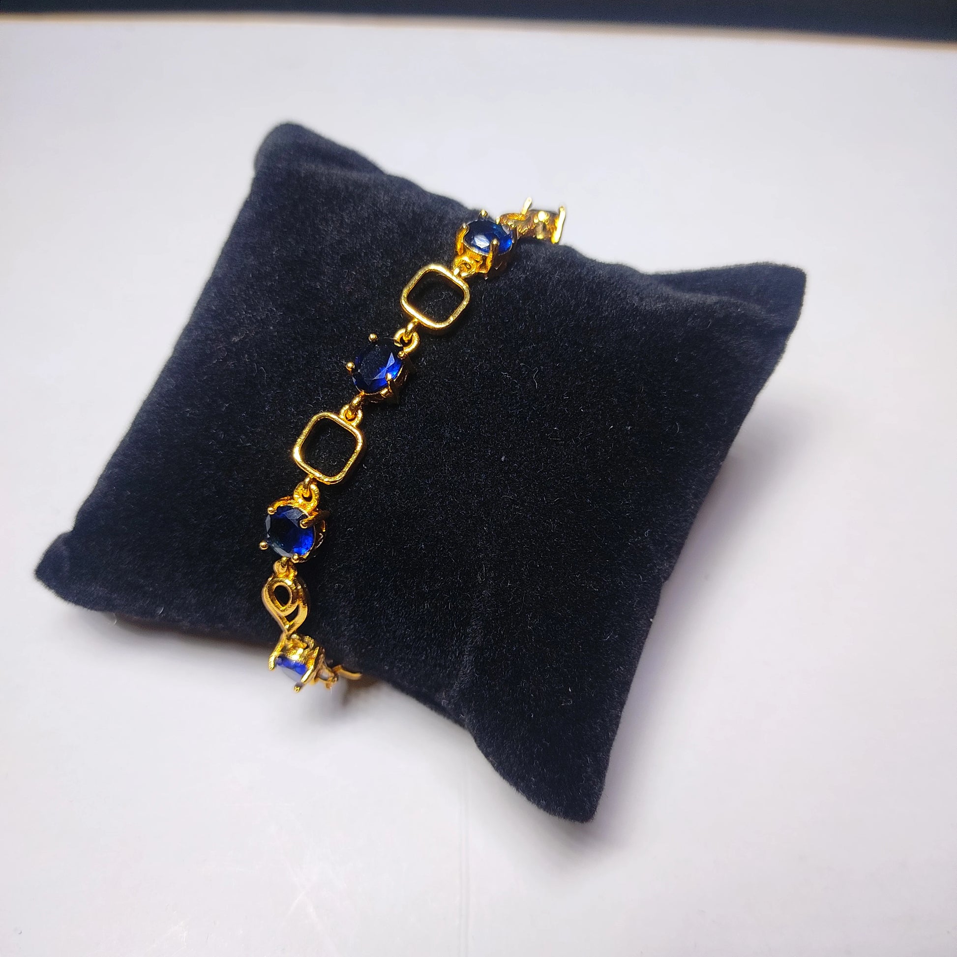 Gold plaated bracelet with blue stones on a black cushion against a white background