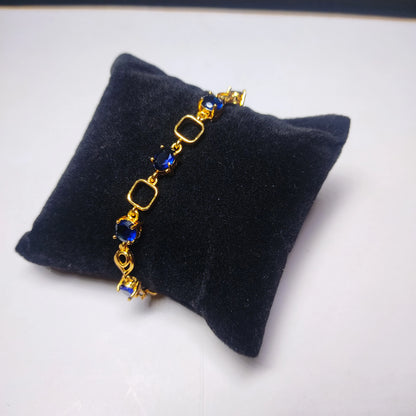Gold plaated bracelet with blue stones on a black cushion against a white background