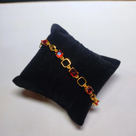 Gold plated bracelet with red gemstones on a black jewelry pillow