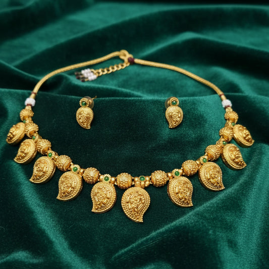 Antique Gold Finish Mango/Manga necklace with green gemstones on a green fabric background