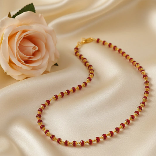 Gold plated Necklace with red crystal beads with gold plated caps on a beige fabric background with a pink rose.