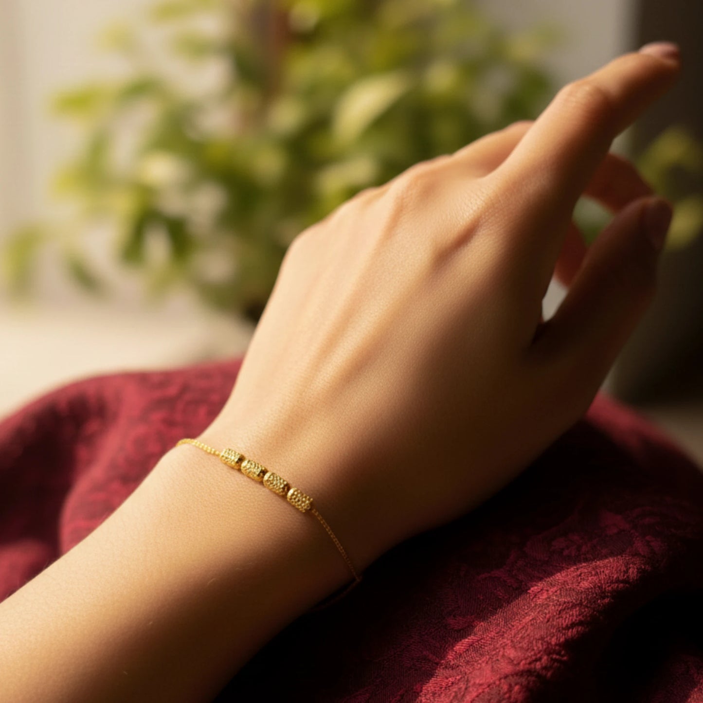 Hand wearing a gold-plated bracelet on a red fabric background with blurred greenery
