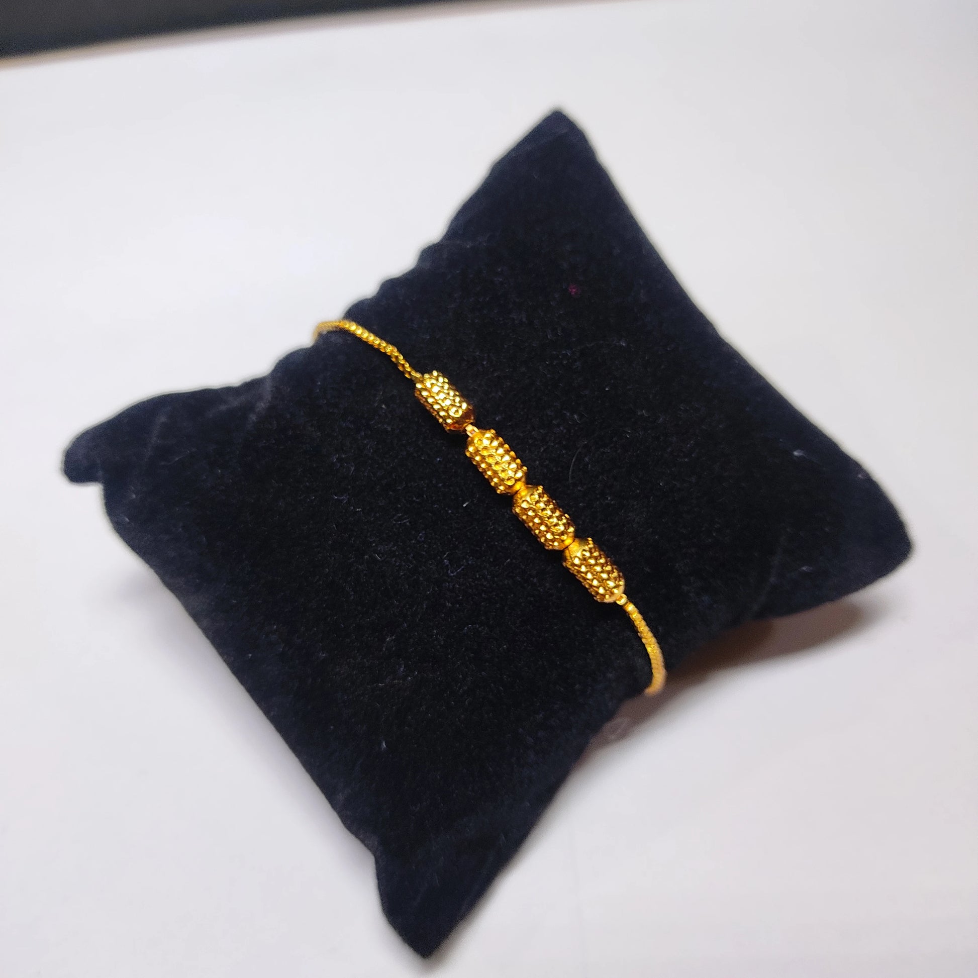 Gold plated bracelet on a black cushion with a white background