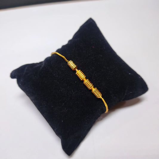Gold plated bracelet on a black cushion with a white background