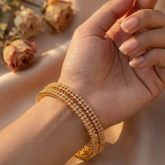 Close-up of a hand wearing a gold plated Bangles with dried flowers in the background