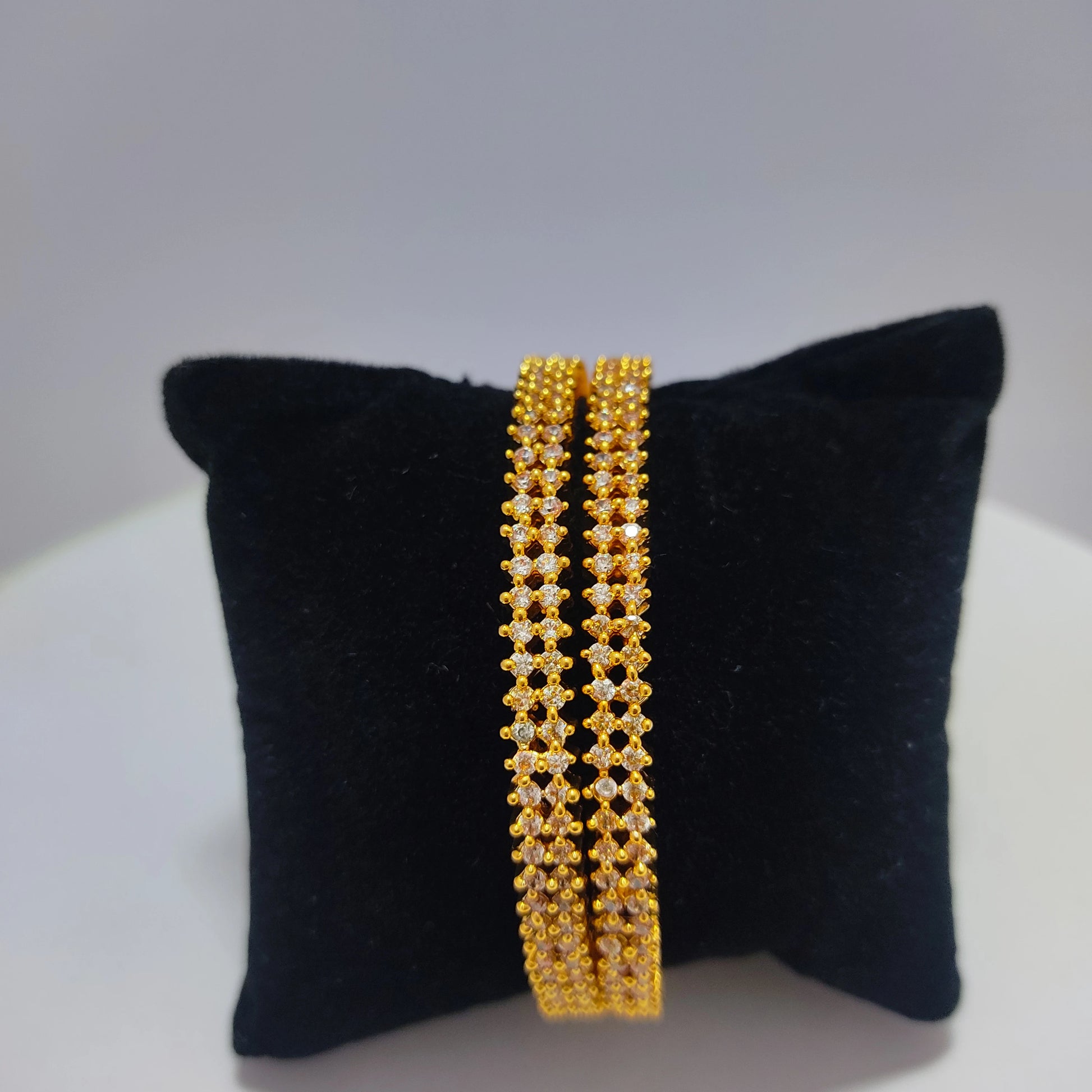 Pair of gold plated bangles on a black cushion with a white background