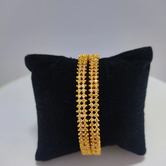 Pair of gold plated bangles on a black cushion with a white background