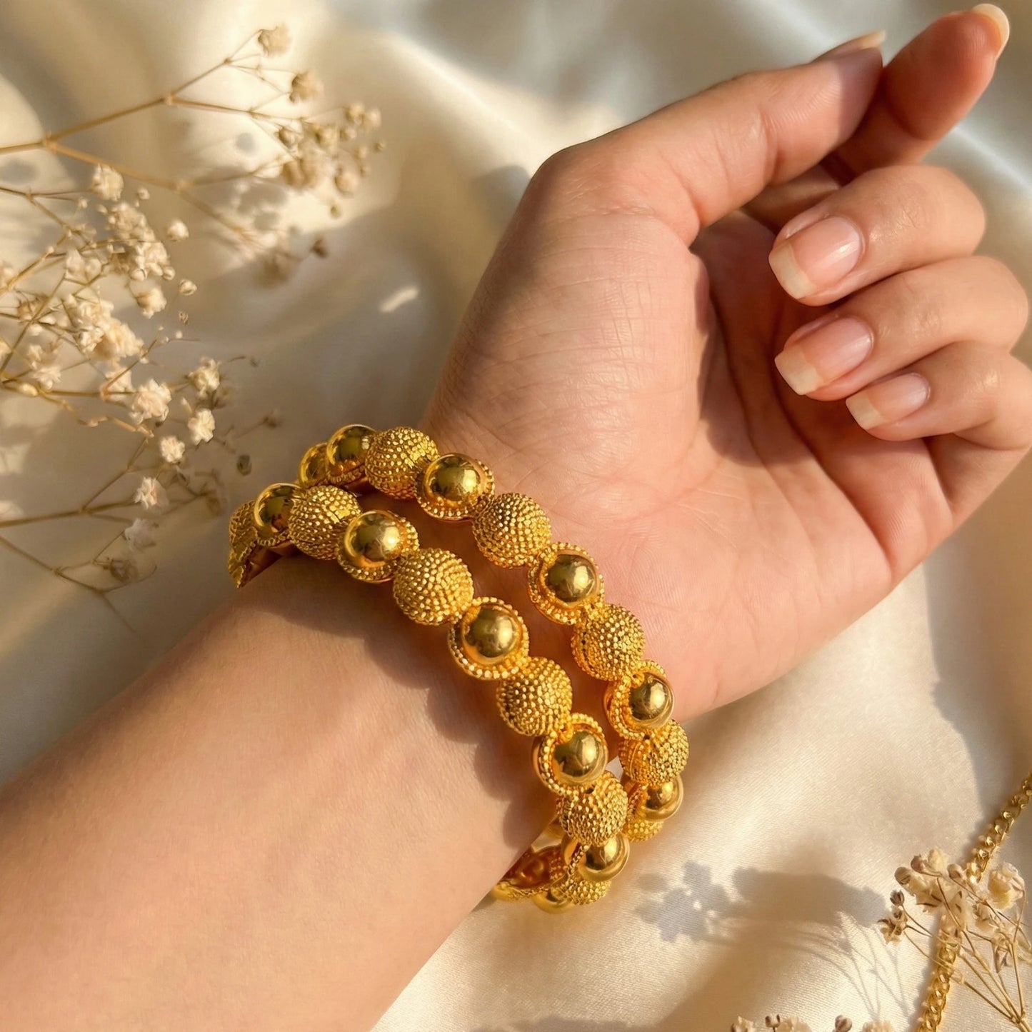 Hand wearing a gold plated bangle set  with a soft background