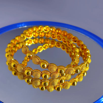 Two gold plated beaded bangles on a reflective surface with a blue rim.