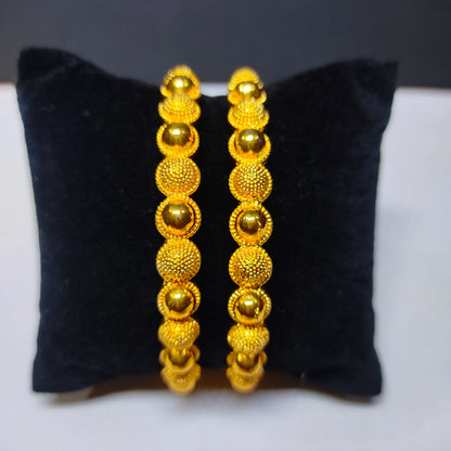 Pair of gold plated beaded bangles on a black cushion