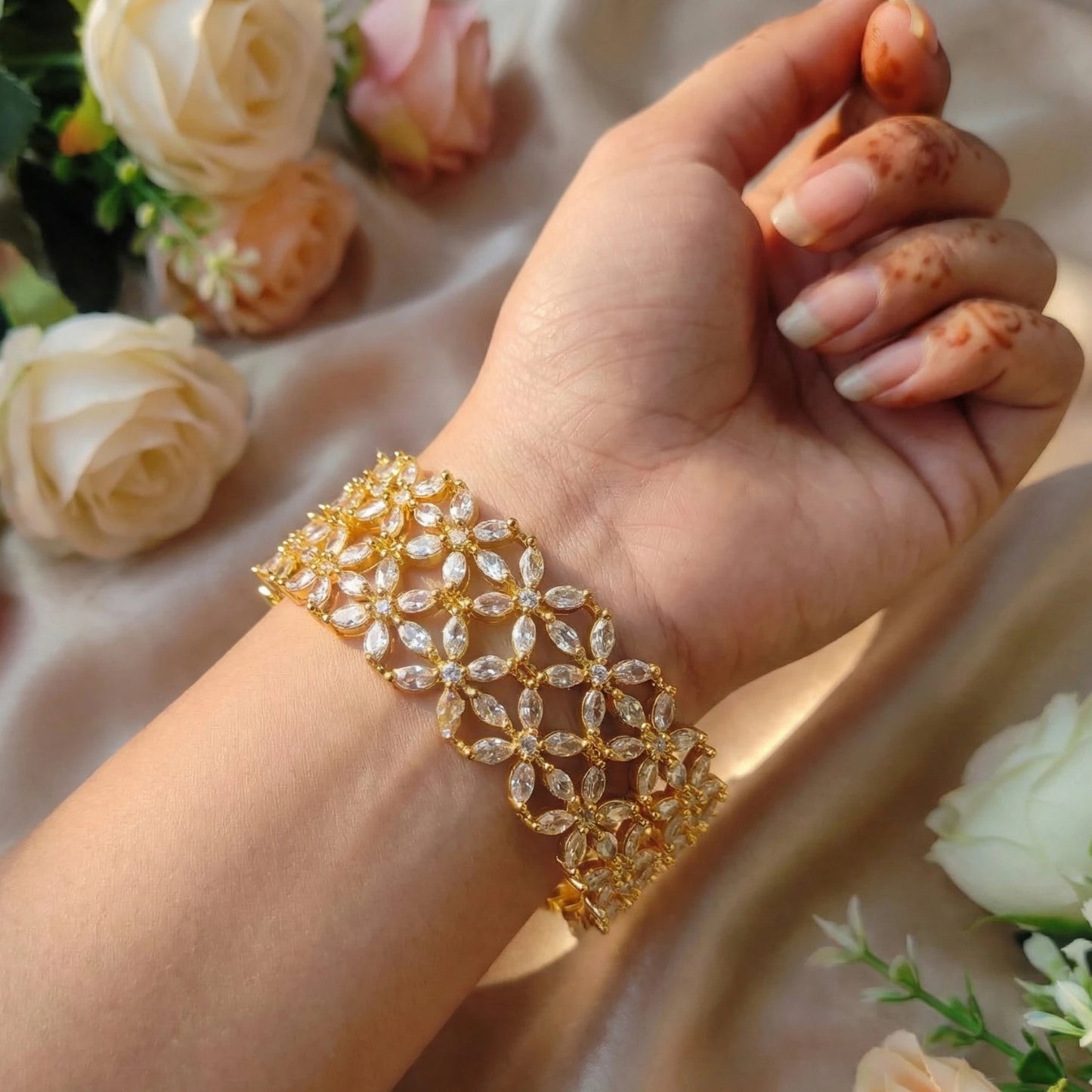 Hand wearing a gold-toned bangle set with floral background
