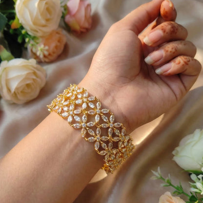 Hand wearing a gold-toned bangle set with floral background