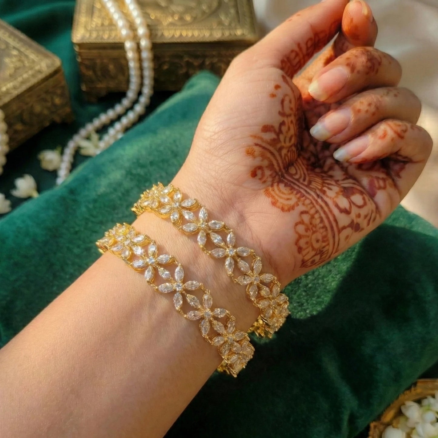 Hand with henna design wearing gold toned bangles on a green fabric background