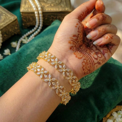 Hand with henna design wearing gold toned bangles on a green fabric background