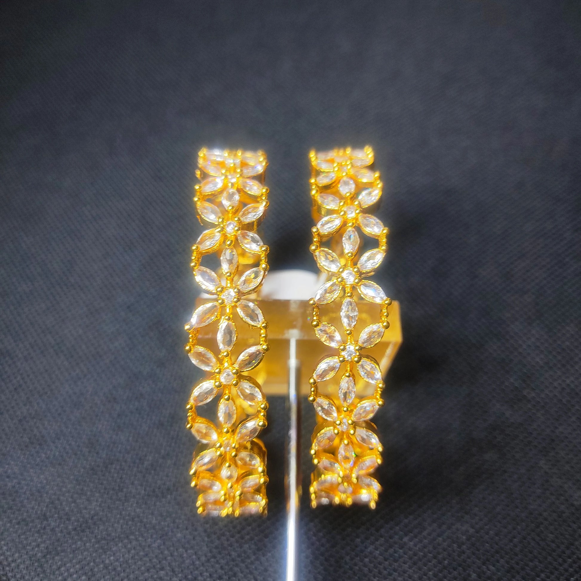 Gold toned set of bangles in floral design with clear stones on a dark background