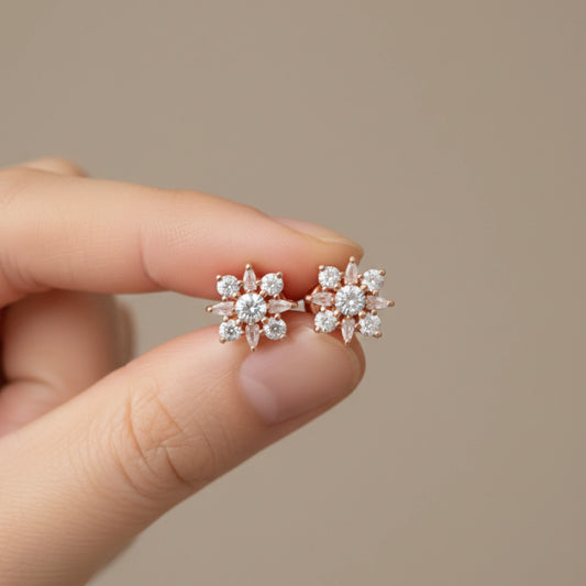 Rose gold floral earrings held between fingers against a neutral background