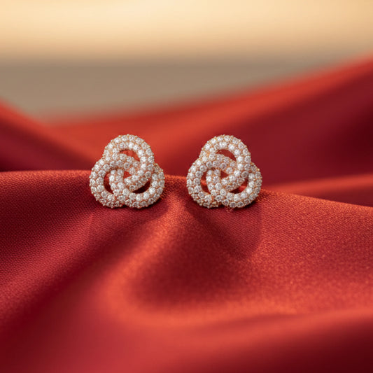 Pair of rose gold earrings with trinity or rose knot details on a red fabric background