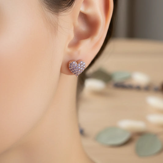 Model wearing a heart shaped rose gold earring with lavender hue stones in a blurred background