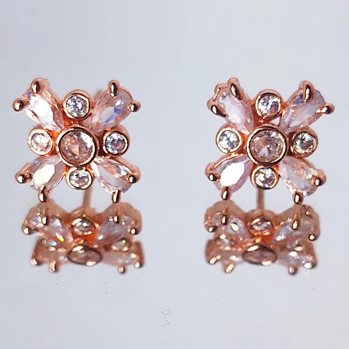 Rose gold flower stud earrings with marquise cut stones on a wooden table background.