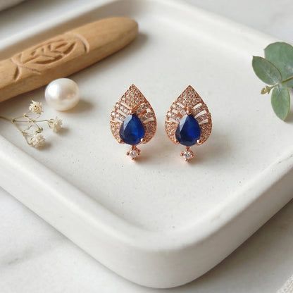 Rose gold earrings with blue gemstones on a white surface