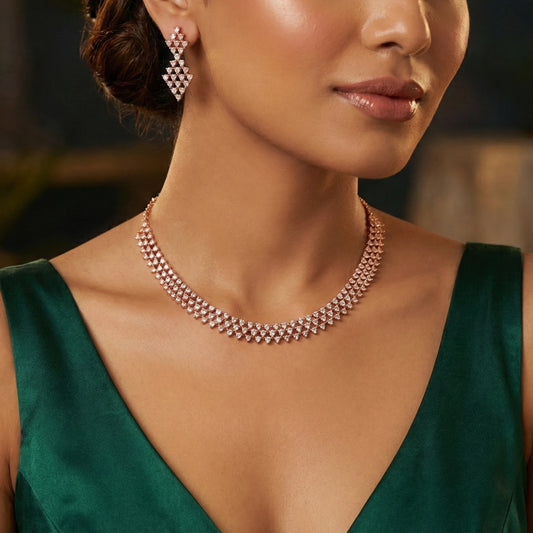 Close-up of a woman wearing a rose gold necklace and earrings with a blurred background