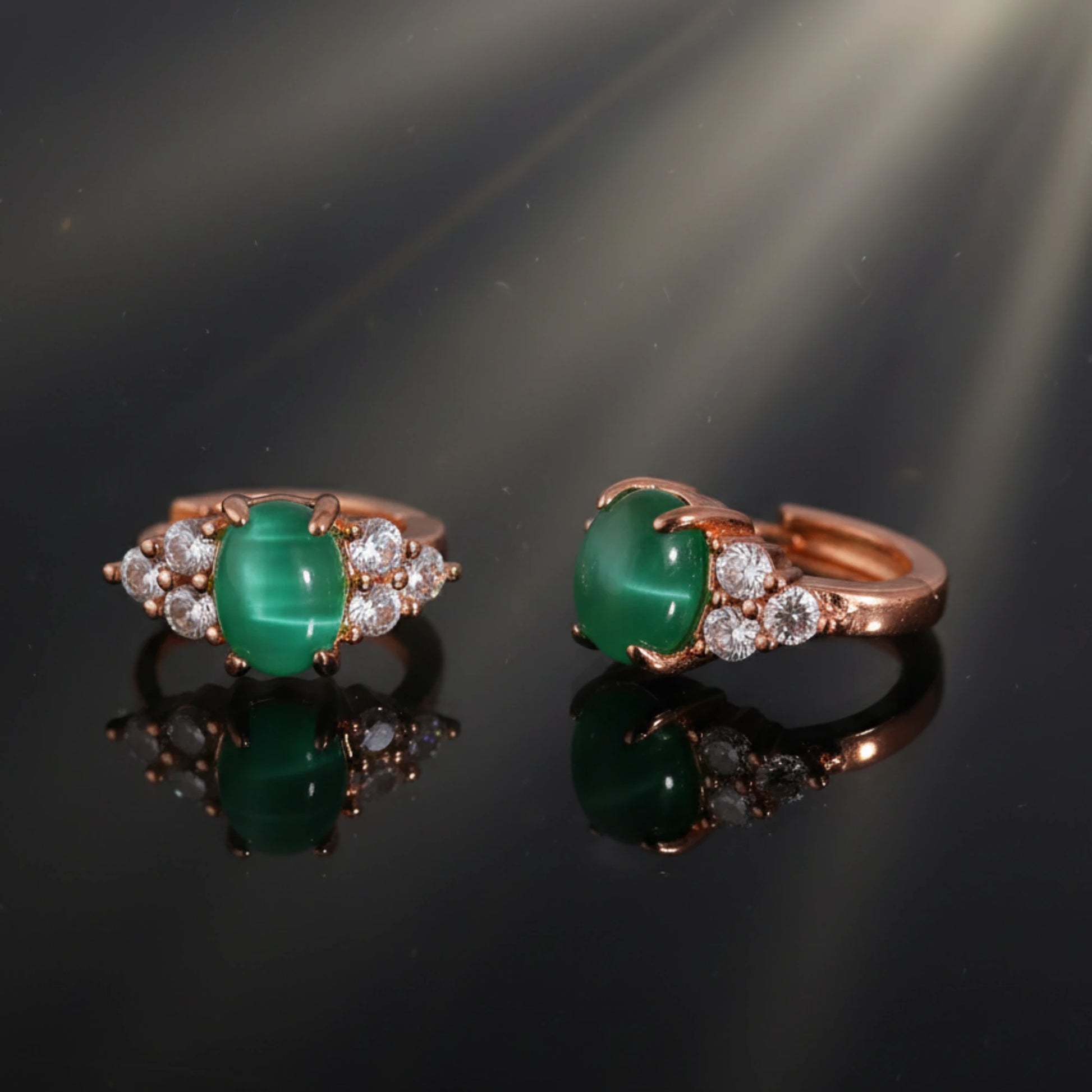 Pair of green gemstone earrings with rose gold and diamond accents on a reflective black surface.
