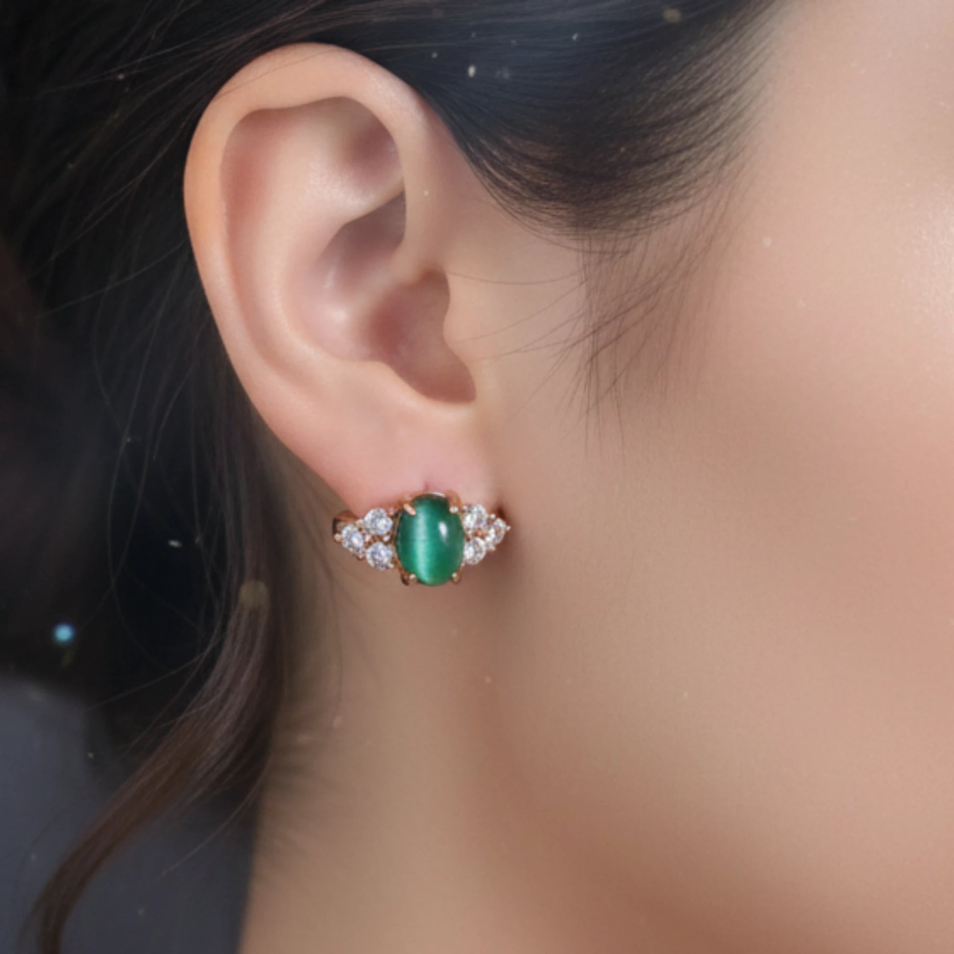 Close-up of an ear wearing a green gemstone earring with a blurred background