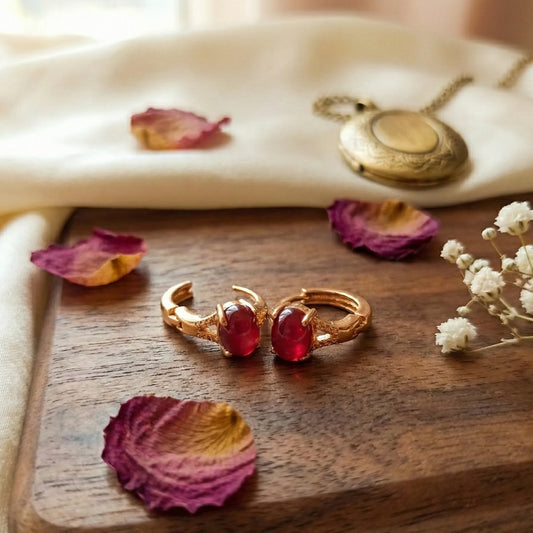 Rose Gold Plated Earrings with red gemstones on a wooden surface with dried flowers