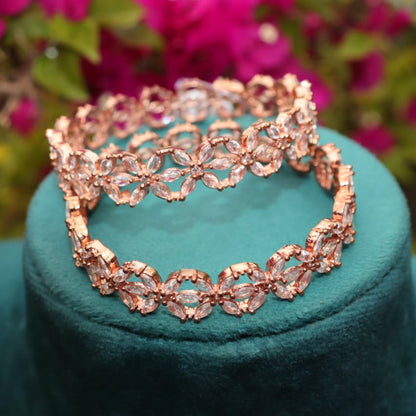 Rose gold bangles on a teal stand with blurred pink flowers in the background