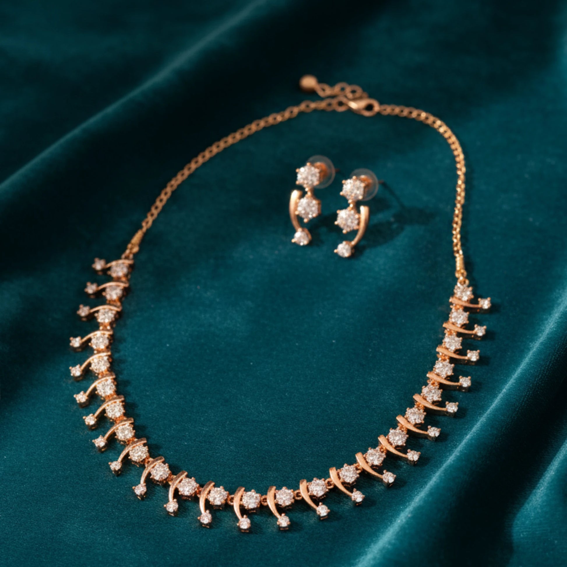 Rose gold necklace and earrings on a teal fabric background