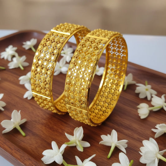 Two gold plated Jali work bangles on a wooden tray with white flowers
