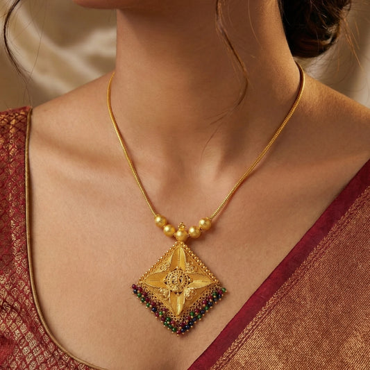 Gold plated necklace with a diamond-shaped pendant worn by a person in a red saree.