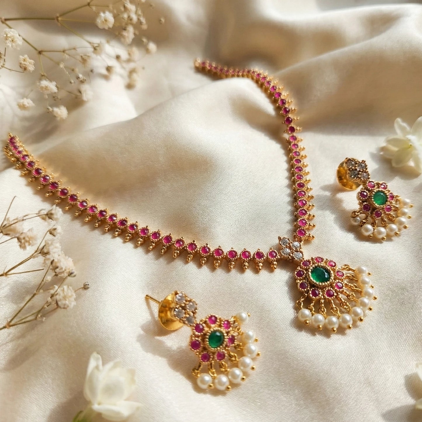 Gold toned jewelry set with pink and green stones on a soft fabric background