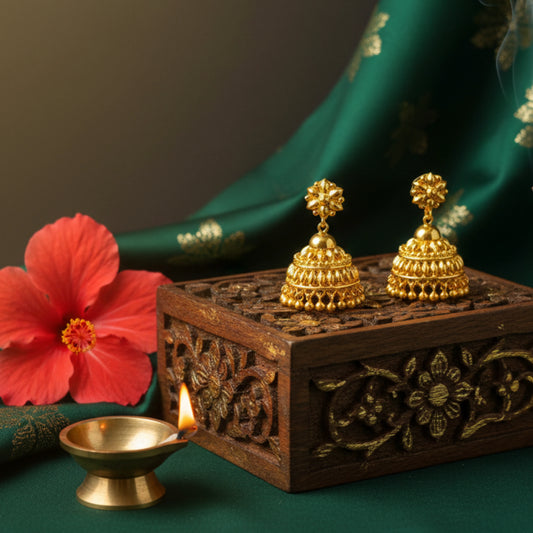 Gold plated earrings on a wooden box with a red flower and lit candle in the background