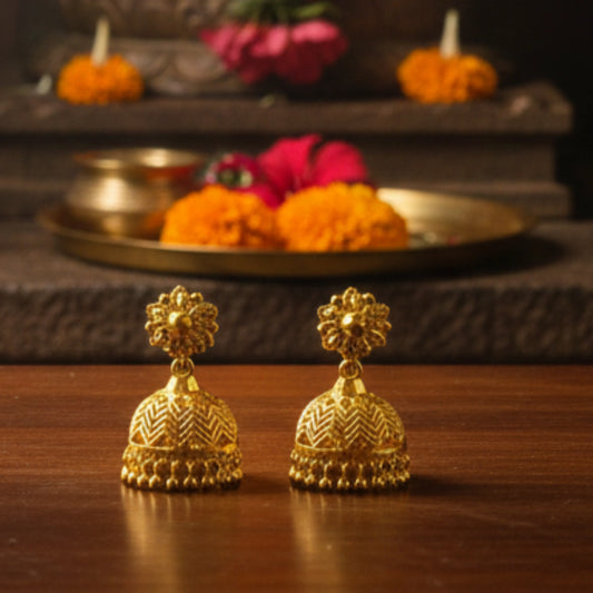 Gold plated earrings on a wooden surface with a blurred background of decorative items.