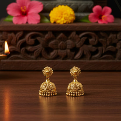 Gold plated earrings on a wooden surface with flowers and a candle in the background