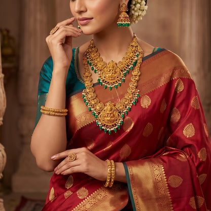 Model wearing 1 long haram, 1 short haram with matching earrings, the design of the harams has goddess lakshmi as the pendant in the center and peacock design on both the sides of the necklace. the embellishments includes different kinds of stones, pearls and green embellishments and are targeted at occasion like weddings, grahapraveshams and festivities