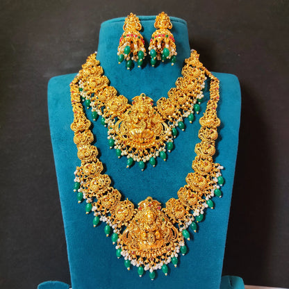 Mannequin highlighting 1 long haram, 1 short haram with matching earrings, the design of the harams has goddess lakshmi as the pendant in the center and peacock design on both the sides of the necklace. the embellishments includes different kinds of stones, pearls and green embellishments and are targeted at occasion like weddings, grahapraveshams and festivities