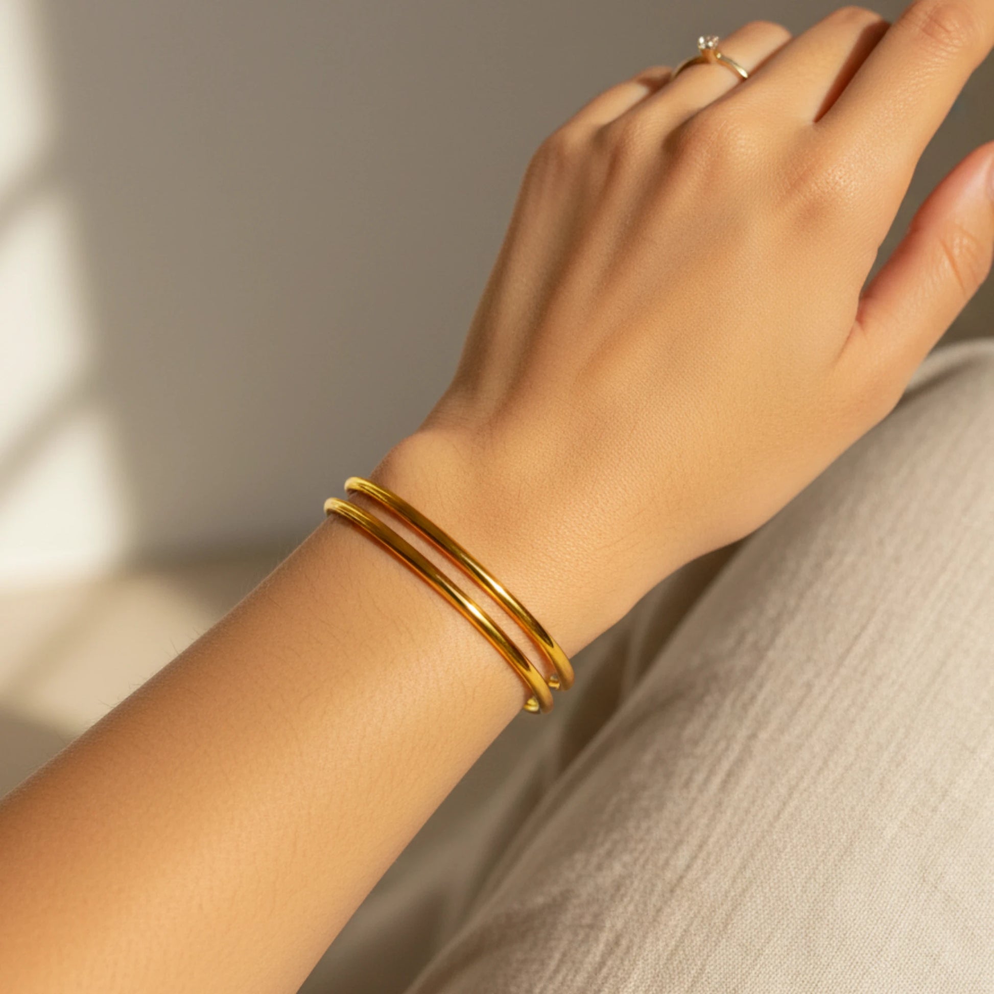 Gold plated minimalist stackable bangles on a wrist with a neutral background