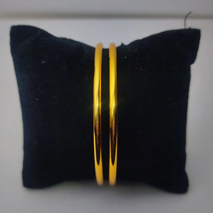 Gold plated minimalist stackable bangle on a black cushion against a white background