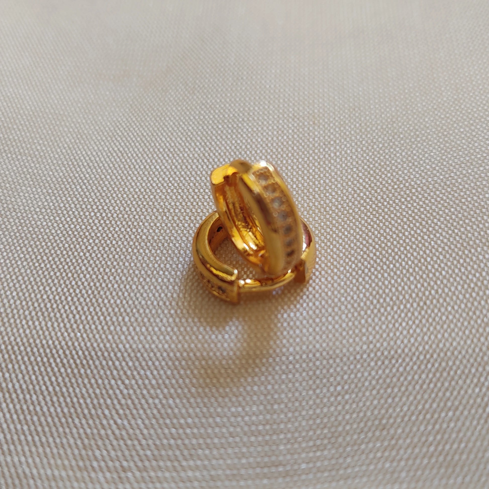 Gold plated second stud hoop earring on a beige fabric background