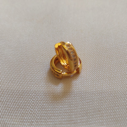 Gold plated second stud hoop earring on a beige fabric background