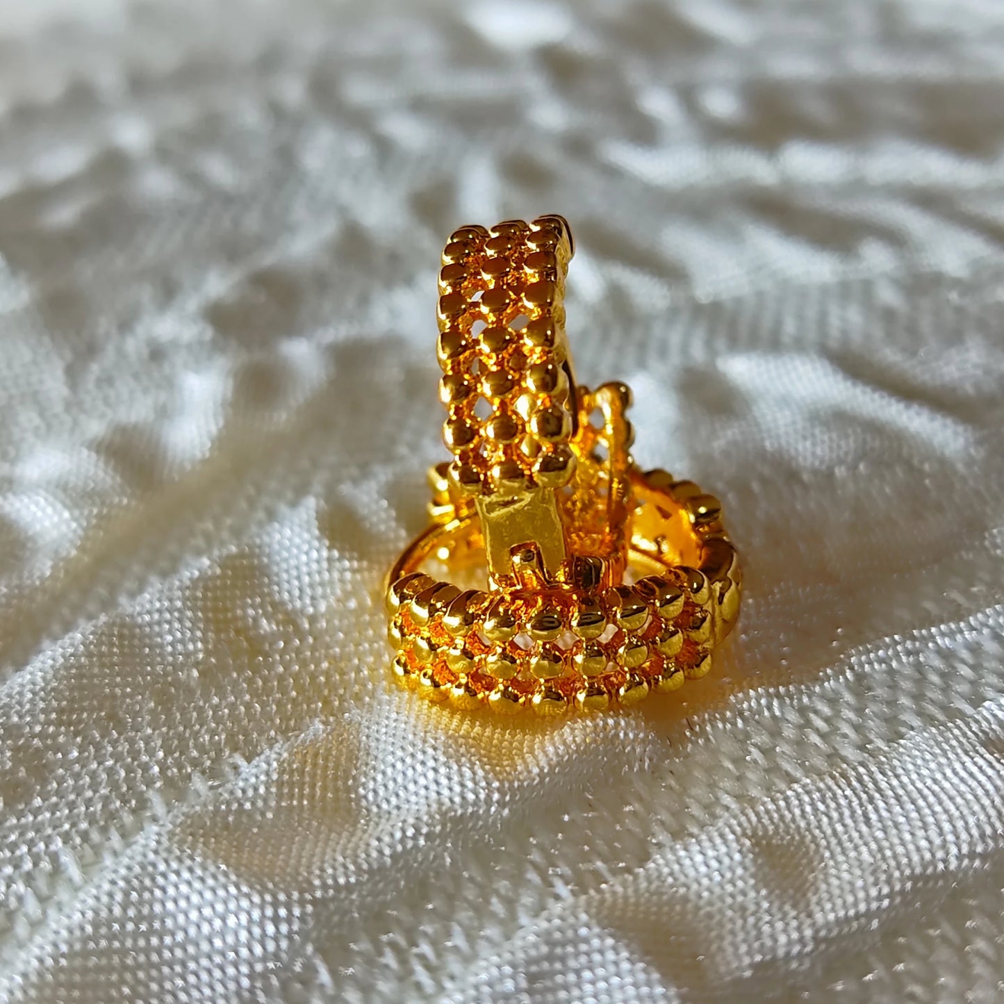 Gold plated second stud ear ring with intricate design on a textured white surface