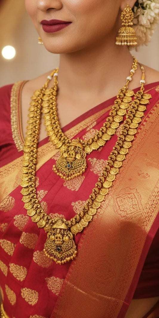 A bride wearing a multi-layered Lakshmi motif antique gold finish temple jewelry set with a red silk saree.