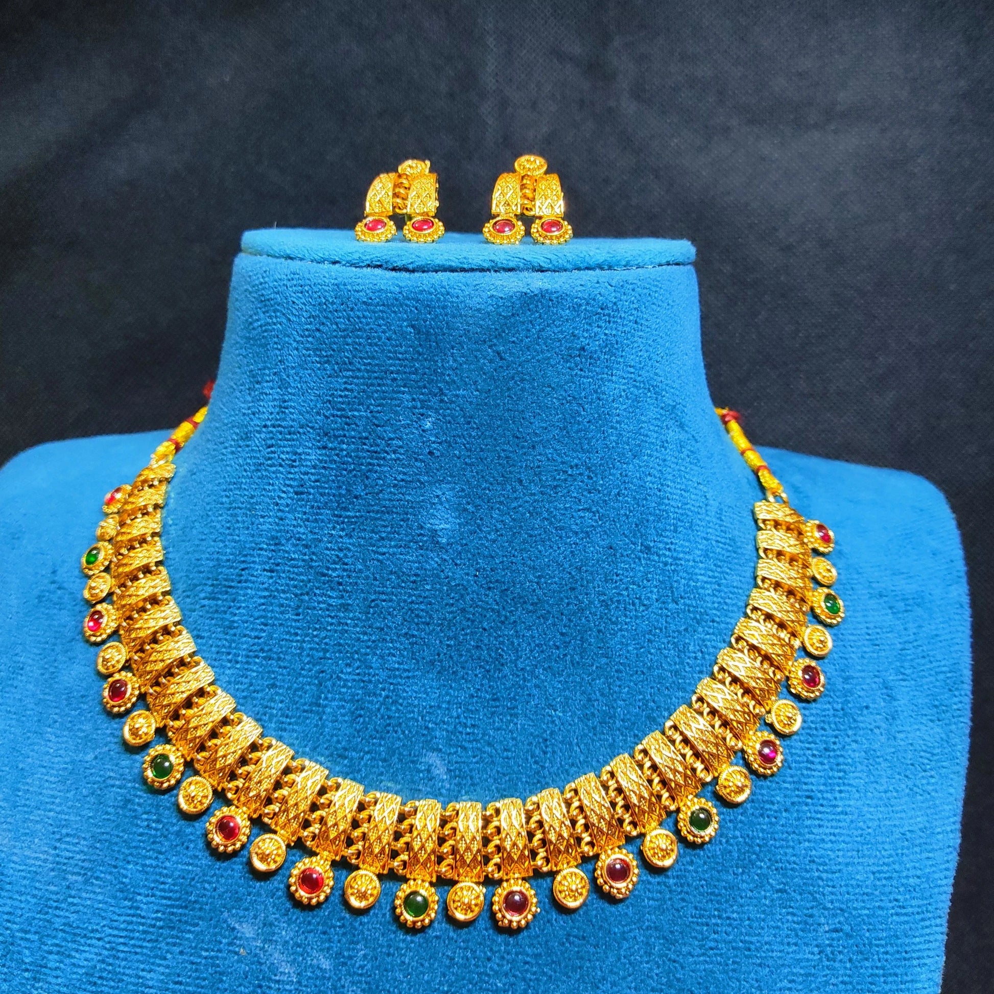 Antique Gold finish necklace and earrings set on a blue velvet mannequin against a dark background