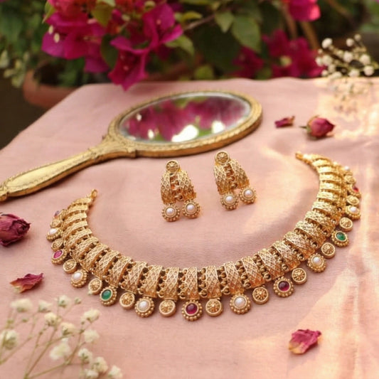 Antique Gold finish necklace and earrings on a pink surface with flowers and a mirror in the background