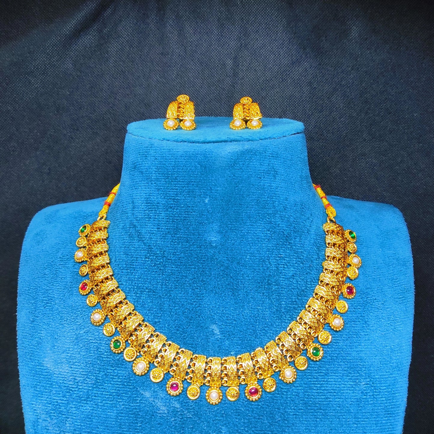 Antique Gold Finish necklace and earrings set on a blue velvet stand against a dark background