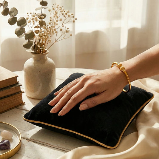 hand with the classic Gold plated kada on a wooden surface with a vase of flowers and books in the background.