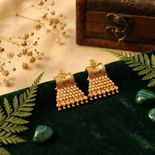 Gold plated earrings on a green fabric background with decorative elements