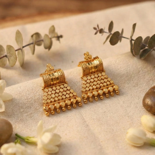 Gold plated earrings on a textured surface with green leaves and flowers